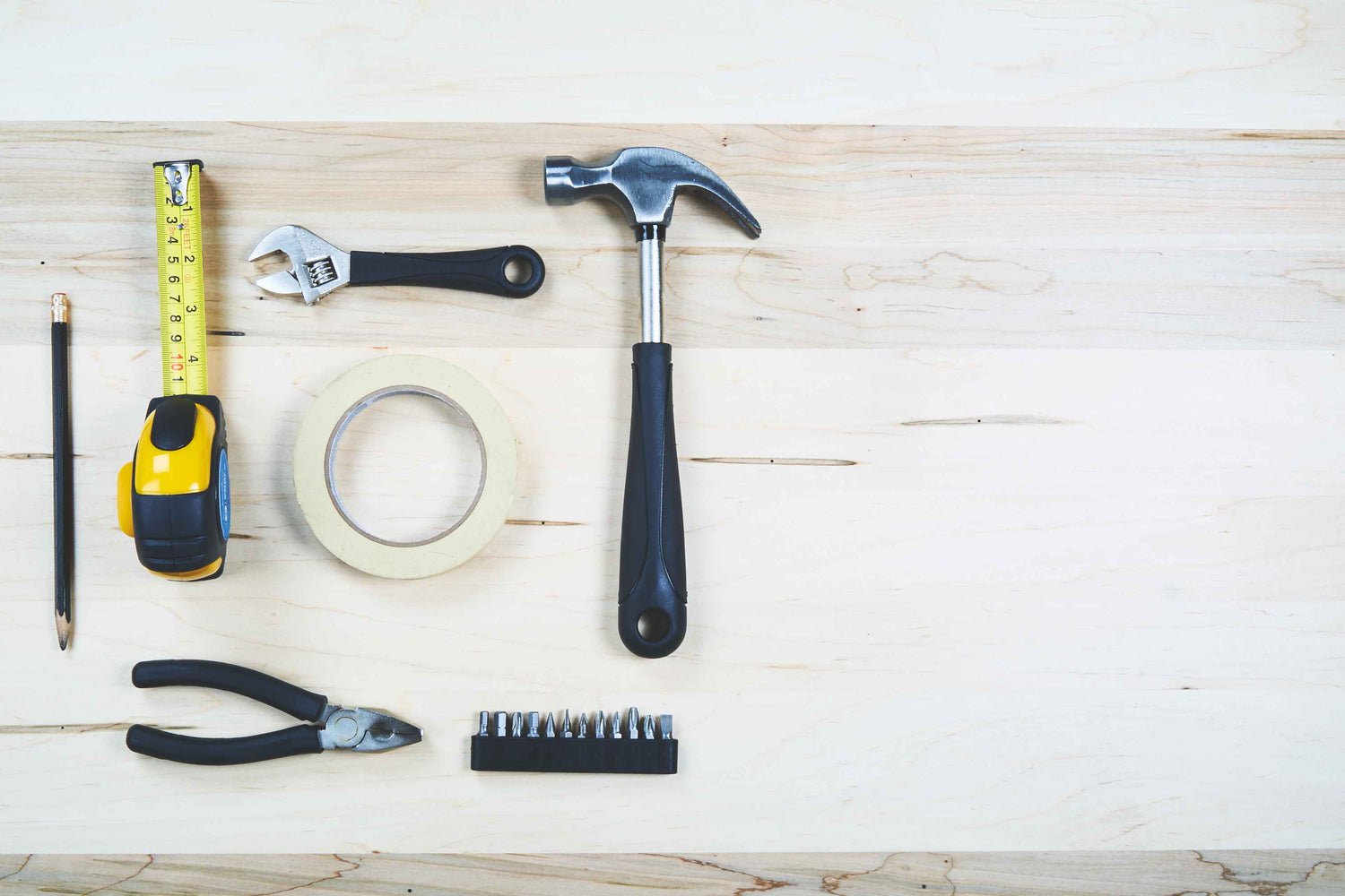 Flatlay von verschiedenen Handwerkzeugen: Hammer, Maßband, Schraubenschlüssel, Zange und Schraubendreher-Bits auf Holzuntergrund.