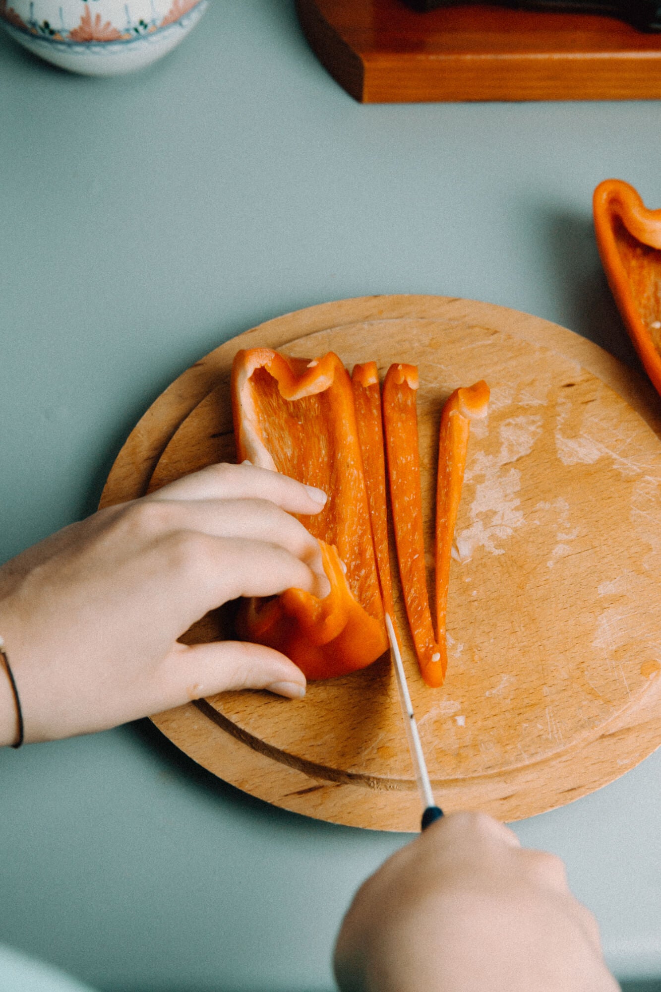 Hände schneiden rote Paprika auf Holzteller, als Symbol für frische Küche und gesunde Zutaten. Inspiration von der Kräuterdrogerie.