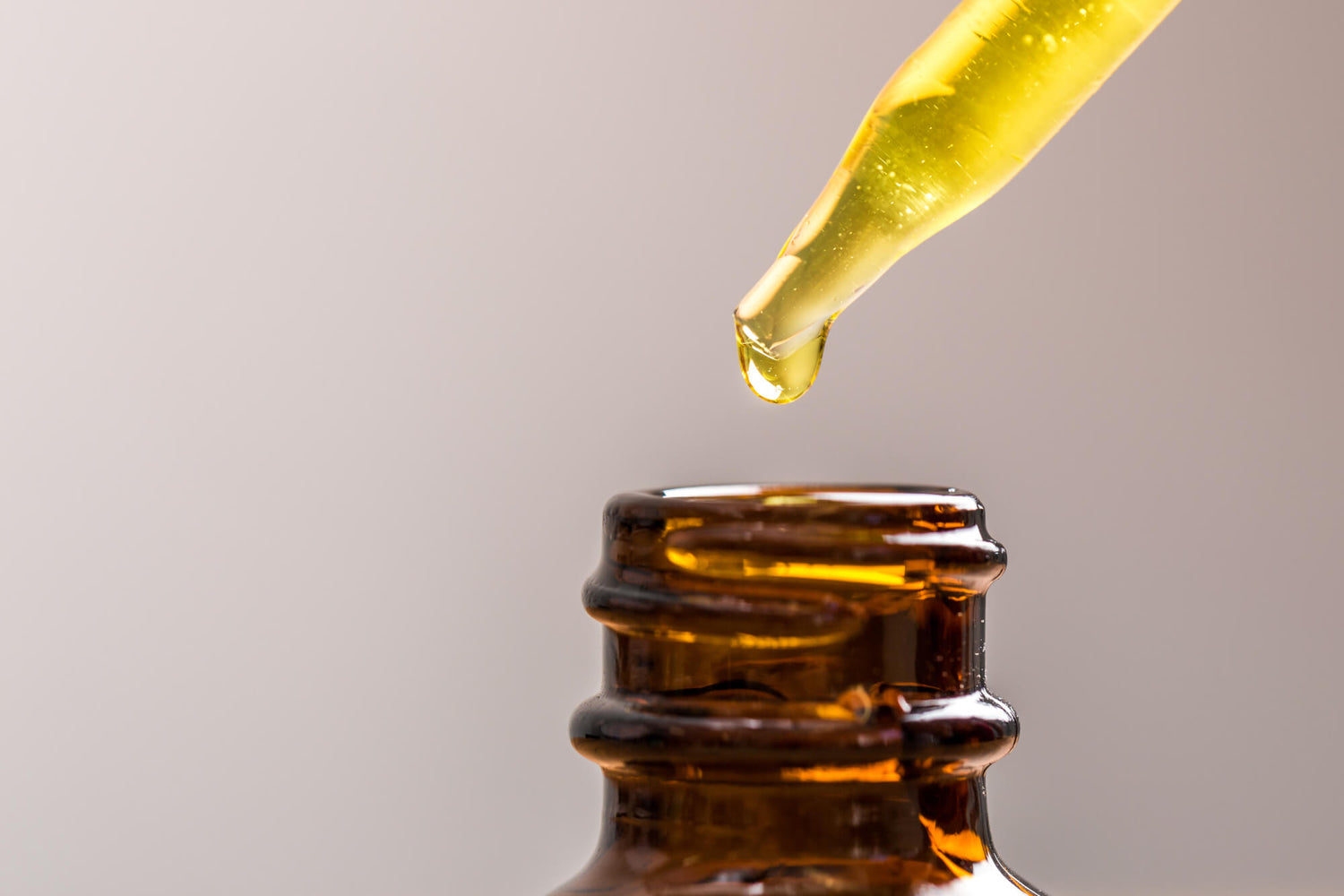 Ein Tropfen gelbes ätherisches Öl oder Serum fällt aus einer Pipette in eine braune Apothekerflasche. Hochwertige Öle und natürliche Kosmetik von der Kräuterdrogerie.