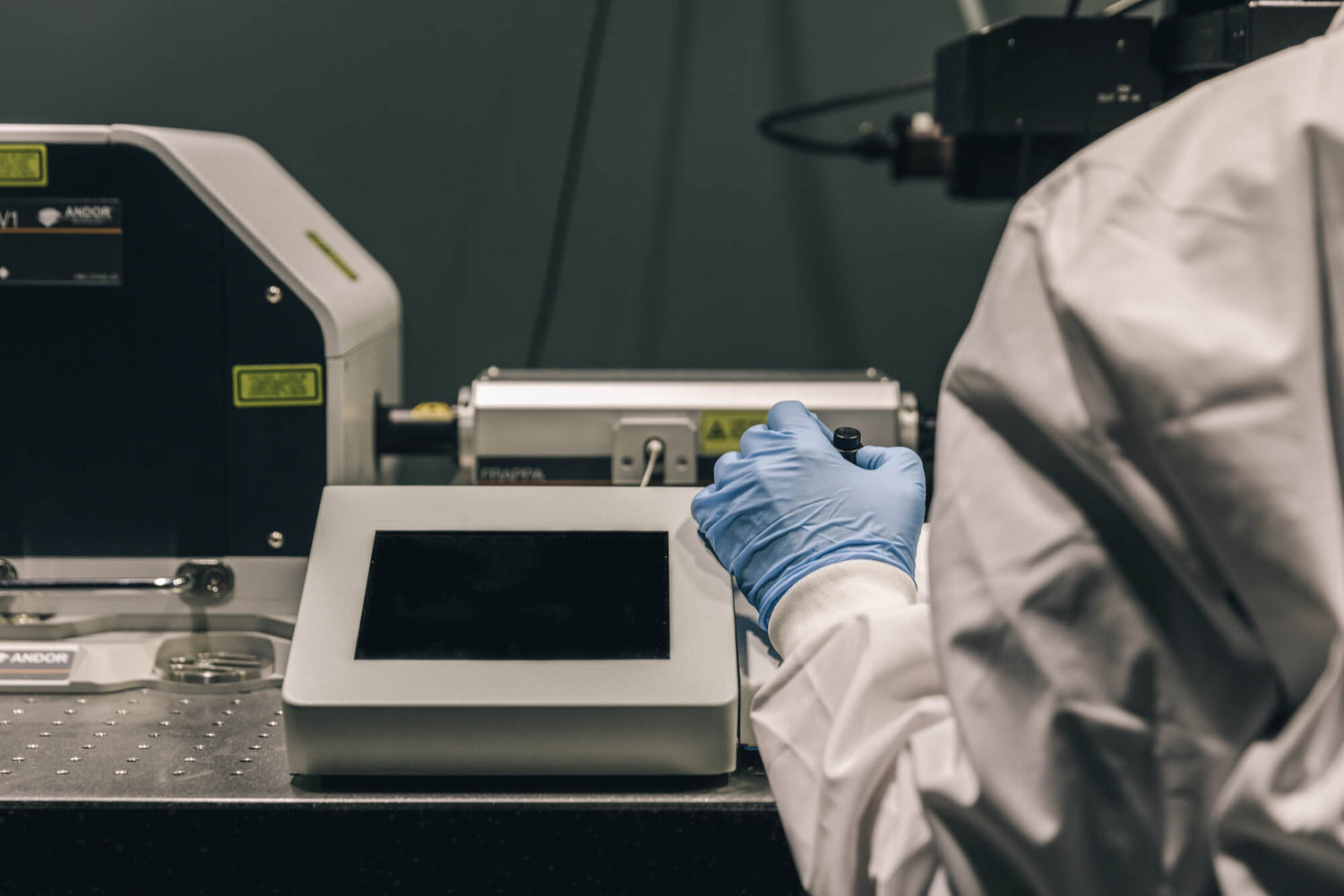 Detailansicht eines Wissenschaftlers in Laborkleidung, der an einem Messgerät arbeitet. Qualitätssicherung, Forschung und Reinheit der Produkte.