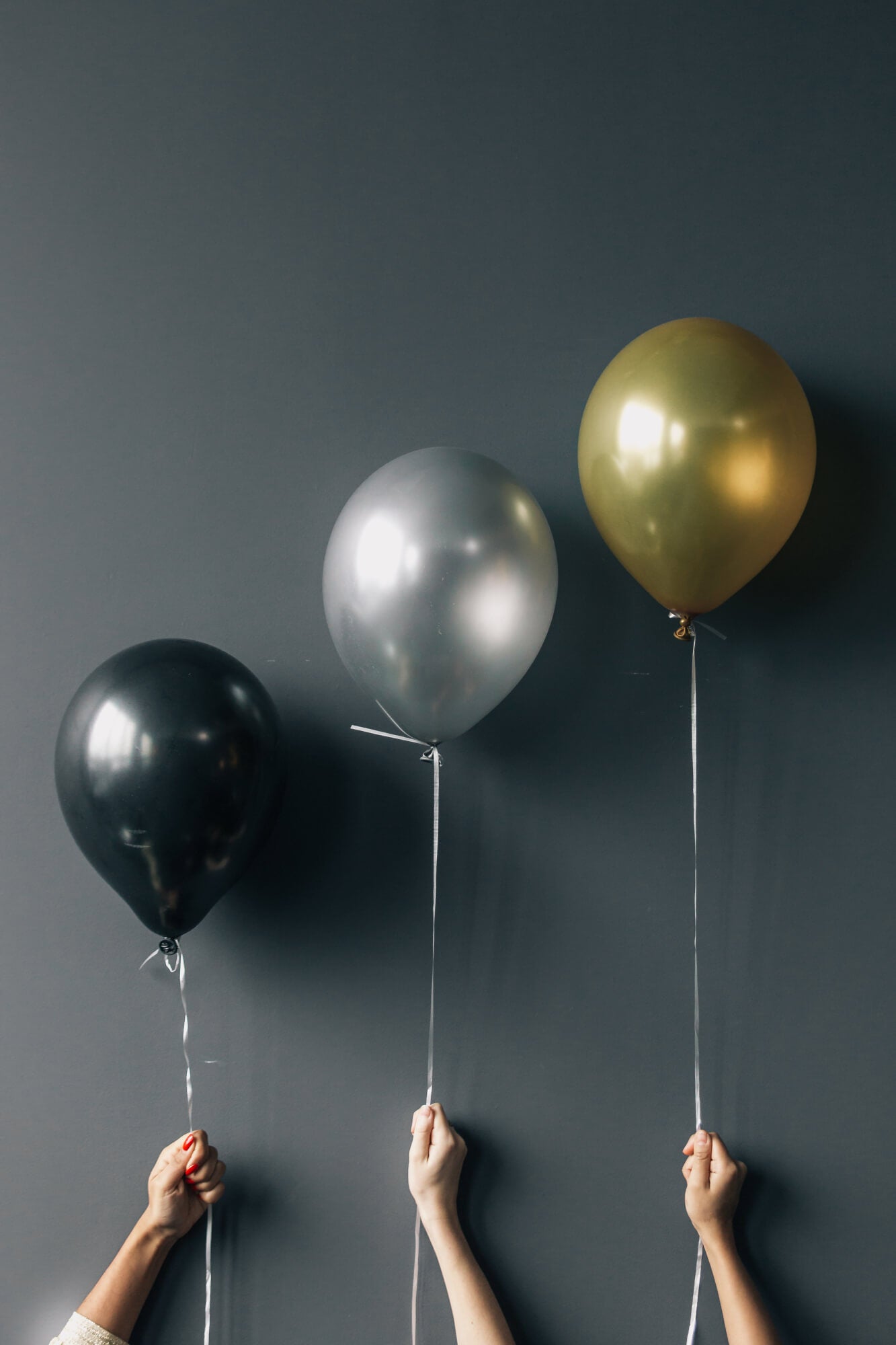 Drei Hände halten schwarze, silberne und goldene Party-Luftballons. Event-Bild für Jubiläen, Rabatte oder festliche Anlässe der Kräuterdrogerie.